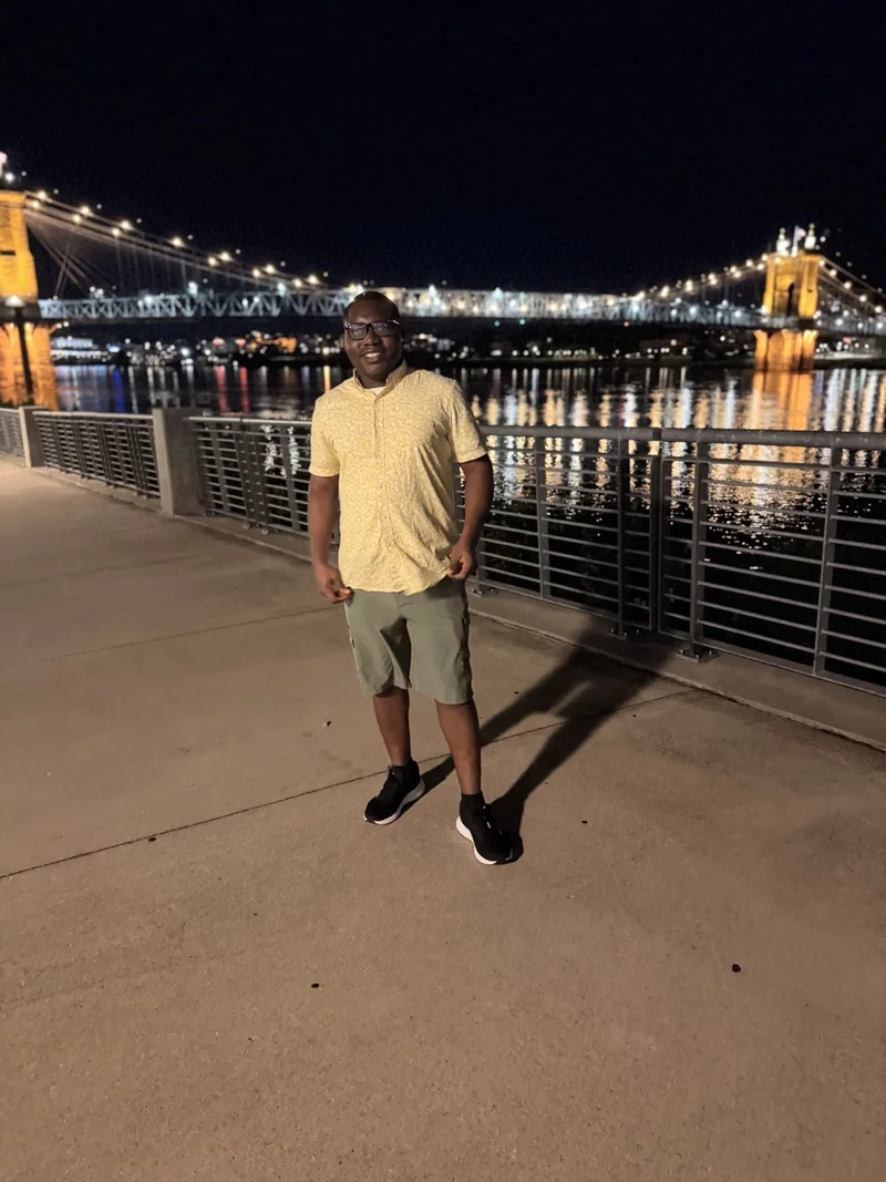 Standing beside the river with an illuminated suspension bridge in the background